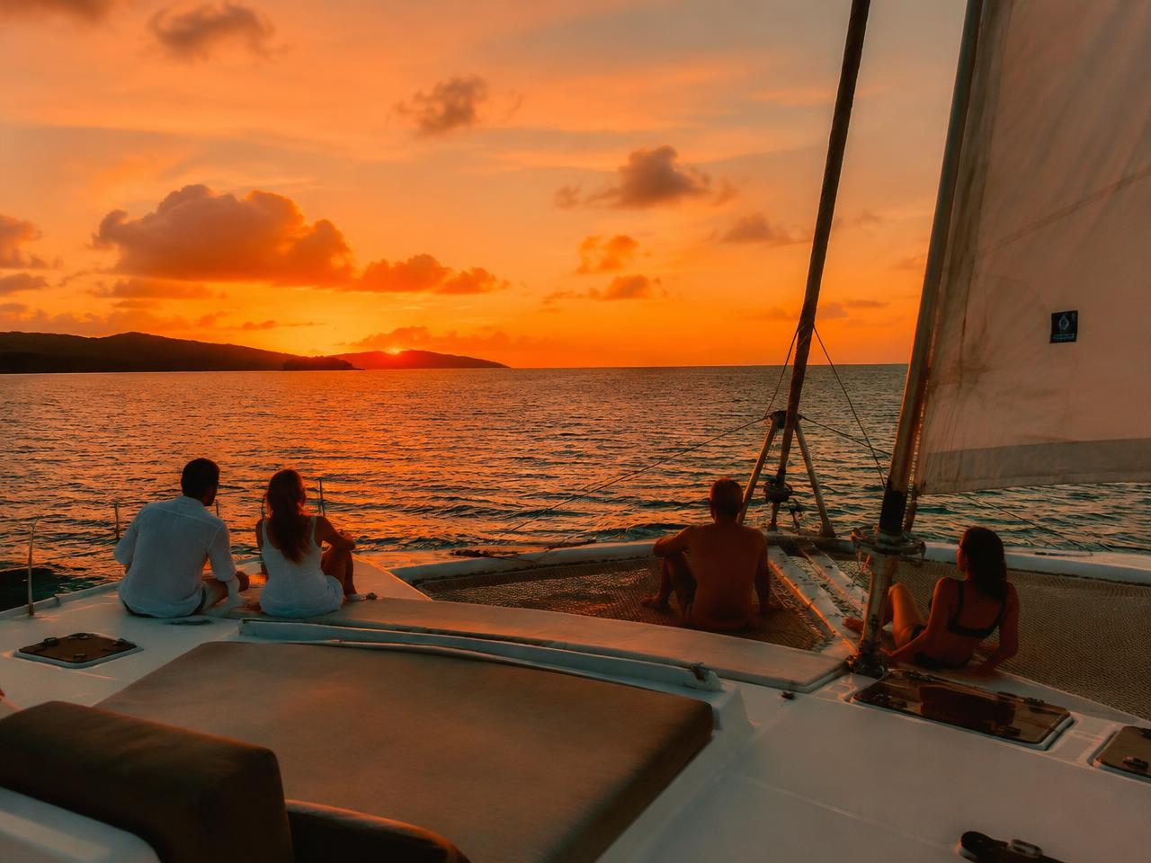 Guests relaxing on the deck of a catamaran sailing toward a Caribbean sunset